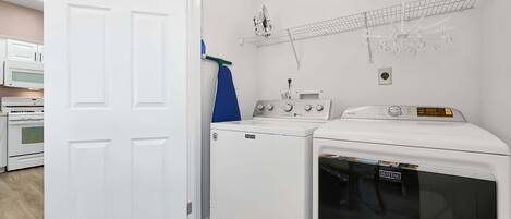 A laundry room with a front-loading washer and dryer, a microwave, and a shelf with hanging items.