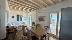 A dining area with a wooden table, chairs, a chandelier, and a view through a glass door. - Panoramic Sea View Villa Near Beach and Town (Mykonos)