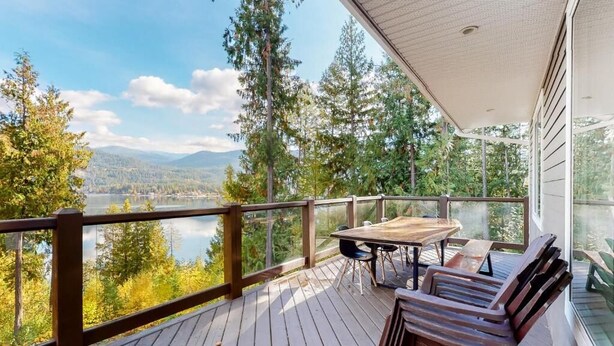 Una terraza de madera con una mesa y sillas, con vista a un lago y un bosque.