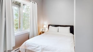 Un dormitorio con cama, mesita de noche, lámpara y ventana con cortinas.