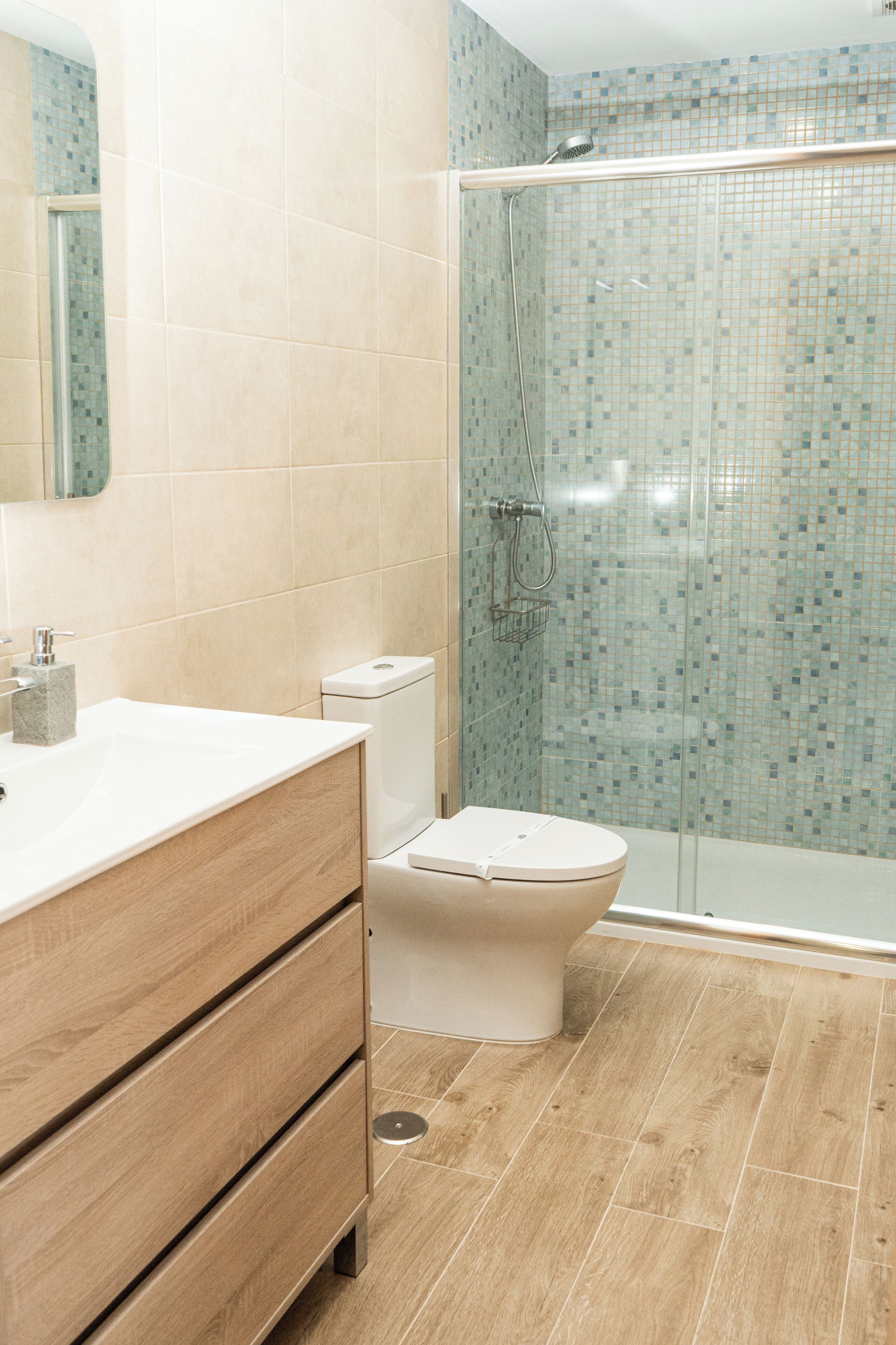 A bathroom with a wooden vanity, a toilet, and a shower area with a glass door.