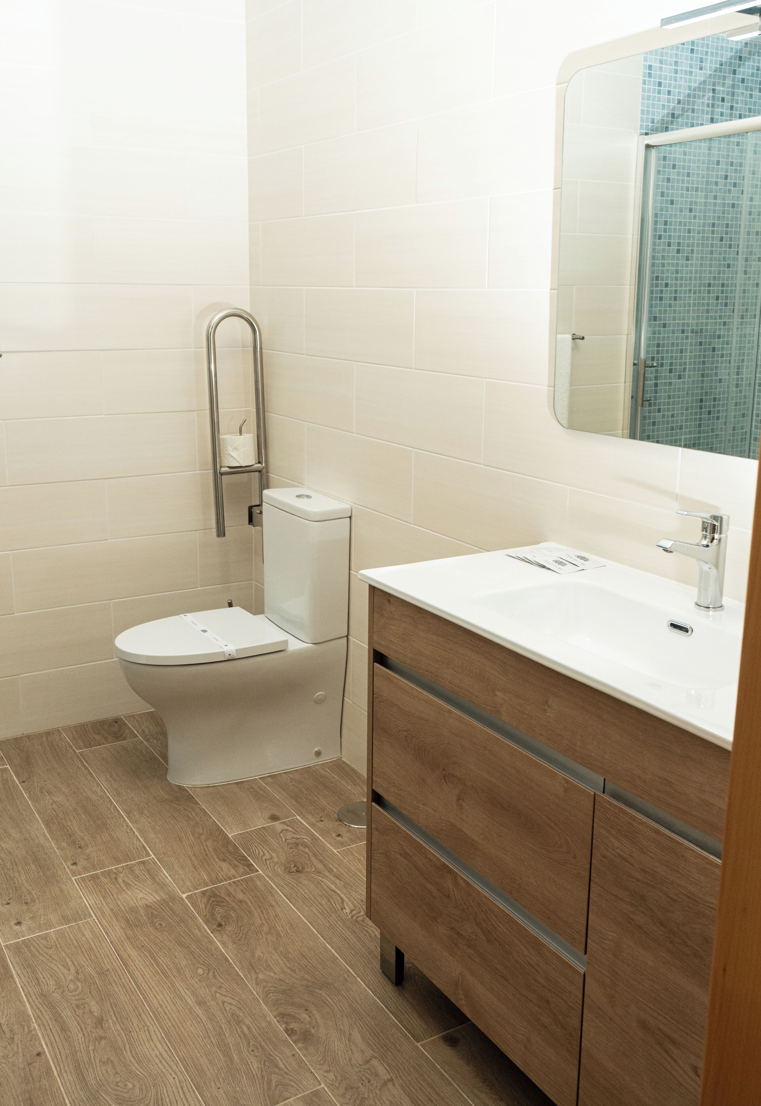 Un baño con inodoro, lavamanos, espejo y tocador de madera.