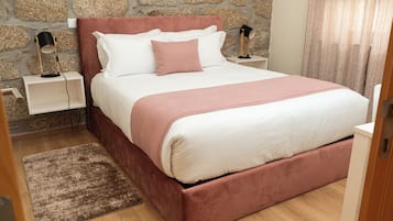 A bedroom with a stone wall, a bed with white and pink bedding, two bedside tables with lamps, and a wooden floor.