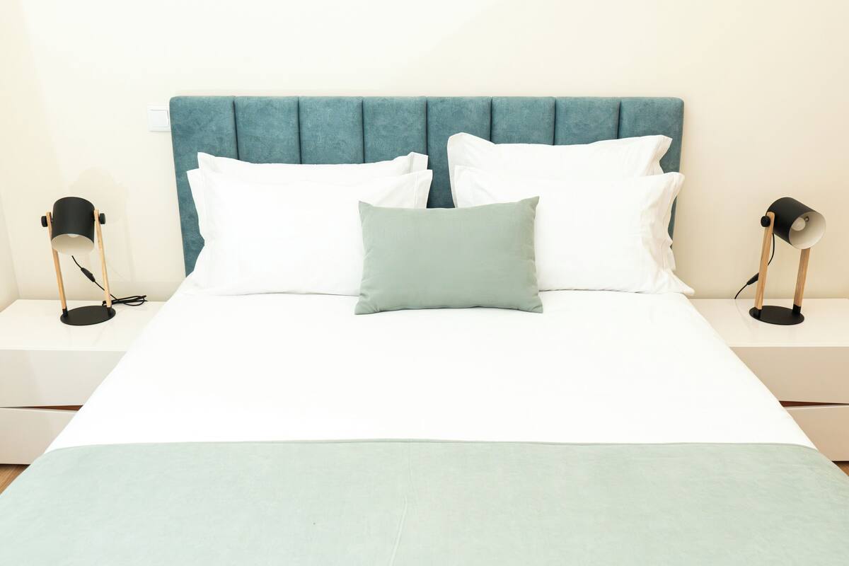 Un lit avec une tête de lit de couleur turquoise, une literie blanche et deux lampes de chevet.