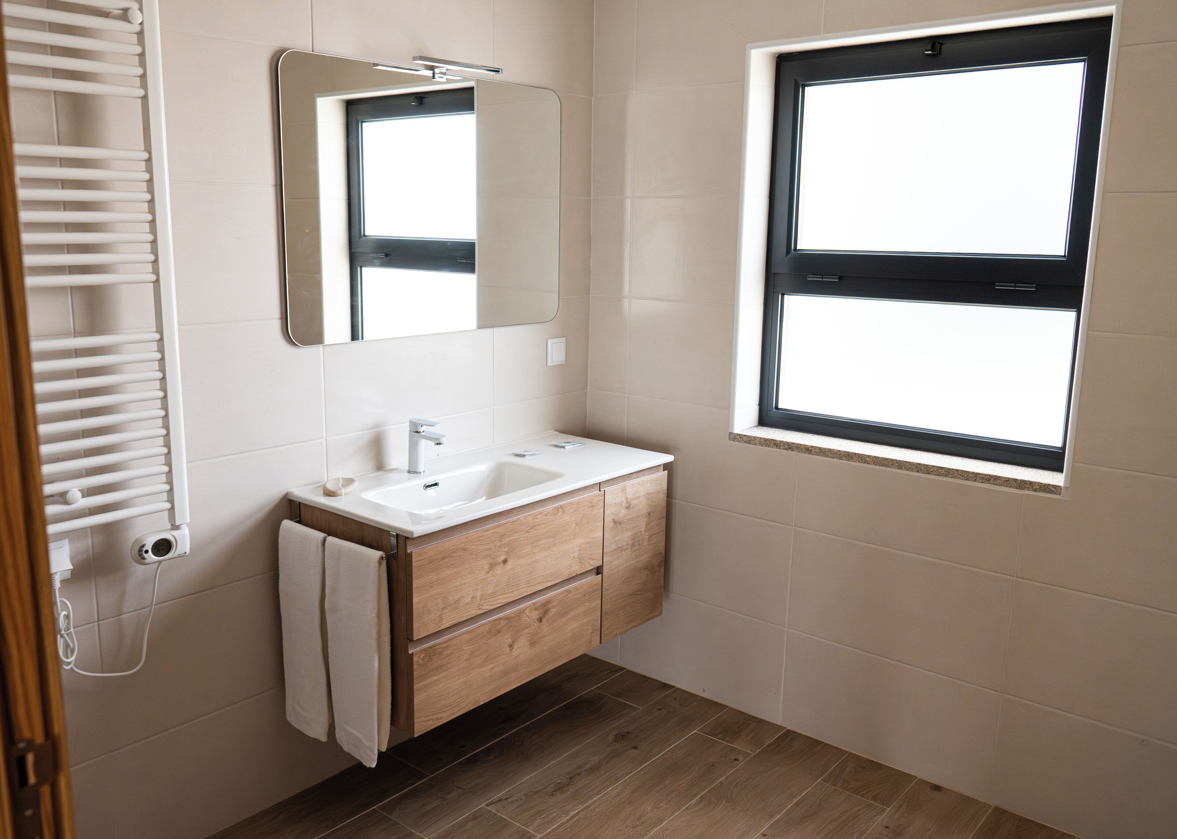 A bathroom with a white sink, wooden vanity, a mirror, a window, and a towel rack.