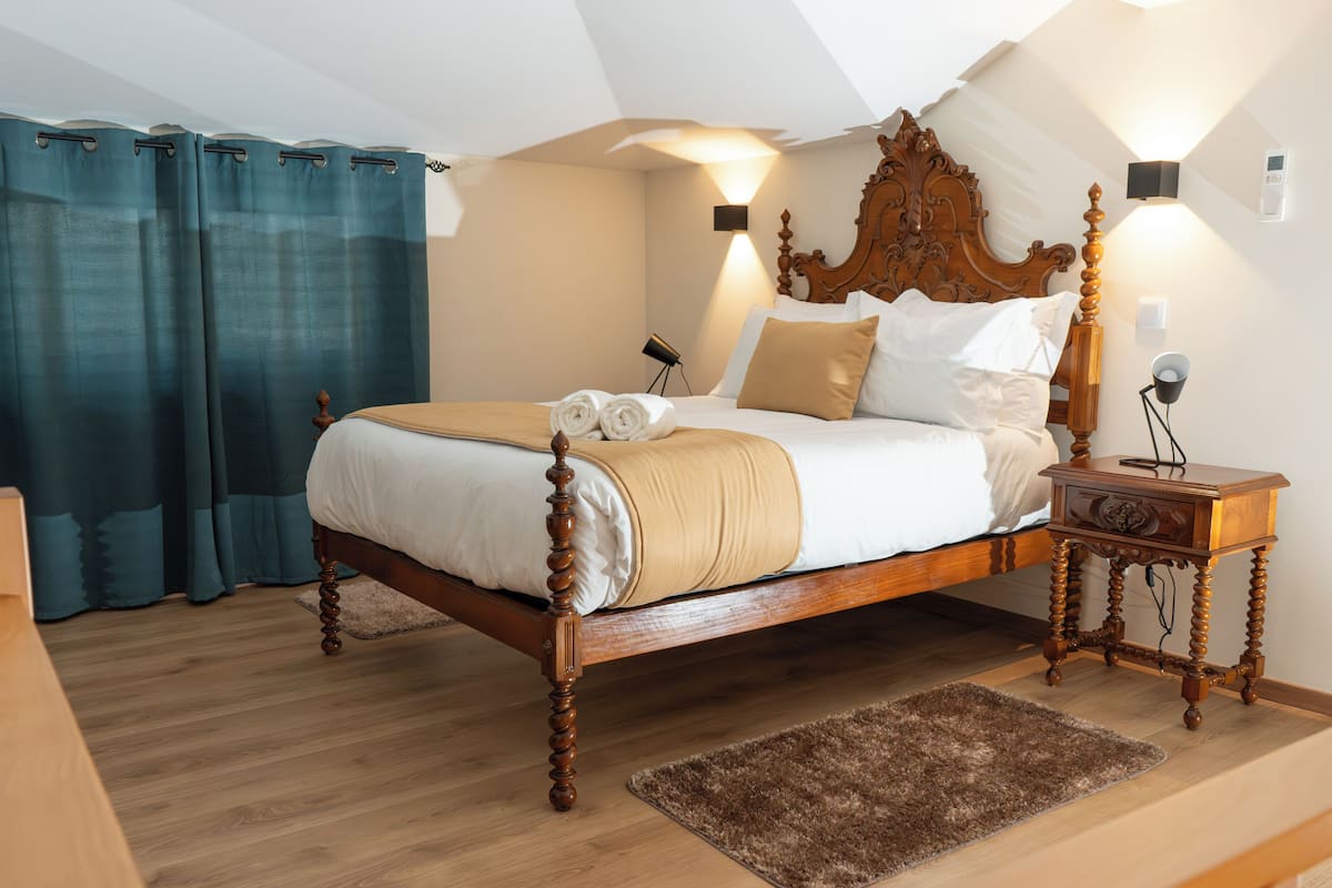 Une chambre à coucher avec un lit en bois, une table de chevet, une lampe de chevet, un luminaire fixé au mur et une fenêtre avec des rideaux.