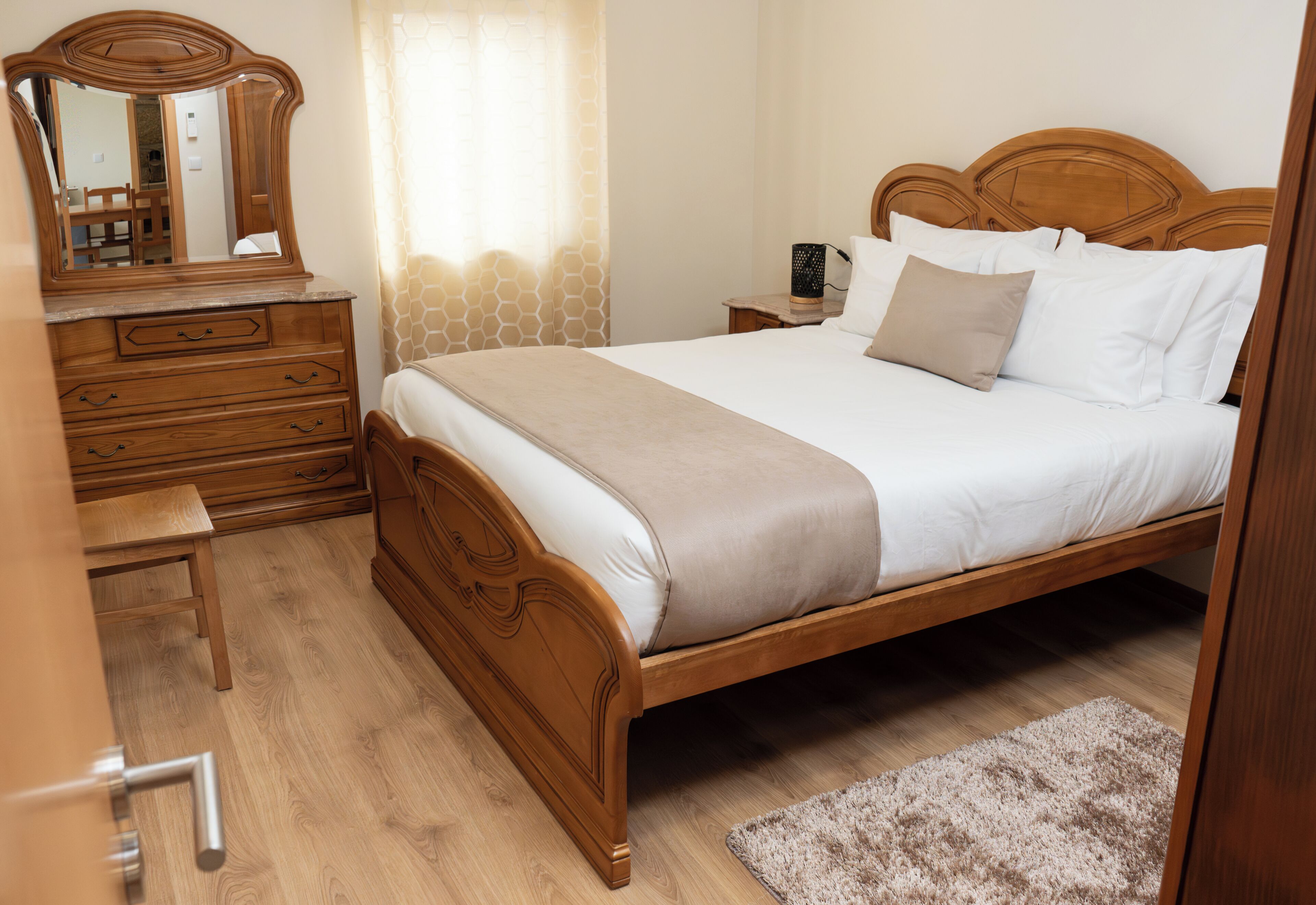 Ein hölzernes Bett mit weißen Leinentüchern, eine Holzkommode, ein Spiegel und ein kleiner Nachttisch.