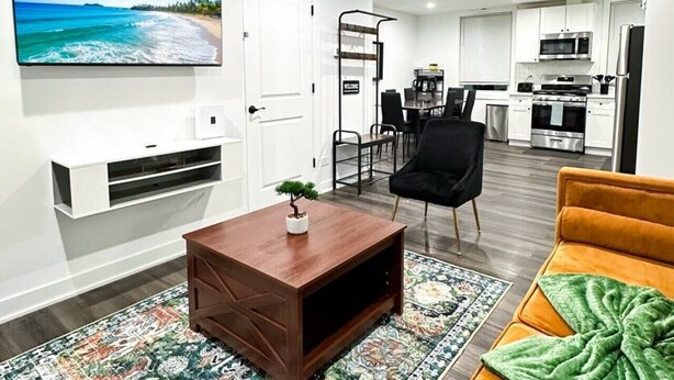 A modern living room with a flat-screen TV, a coffee table, a sofa, and a kitchen in the background. - Modern Berwyn Retreat - 15 Min to Midway - Easy Access to Chicago (Berwyn)