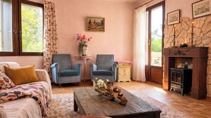 A cozy living room with a sofa, two armchairs, a coffee table with a decorative centerpiece, a fireplace, and a stone wall. - Maison de maître en Provence - Charming and old-fashioned in the countryside (Beaucaire)
