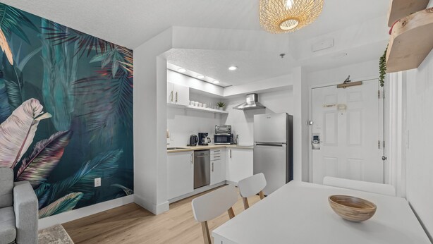 Een moderne keuken met witte kastjes, een magnetron en een koelkast. Er is een eethoek met een witte tafel en stoelen.