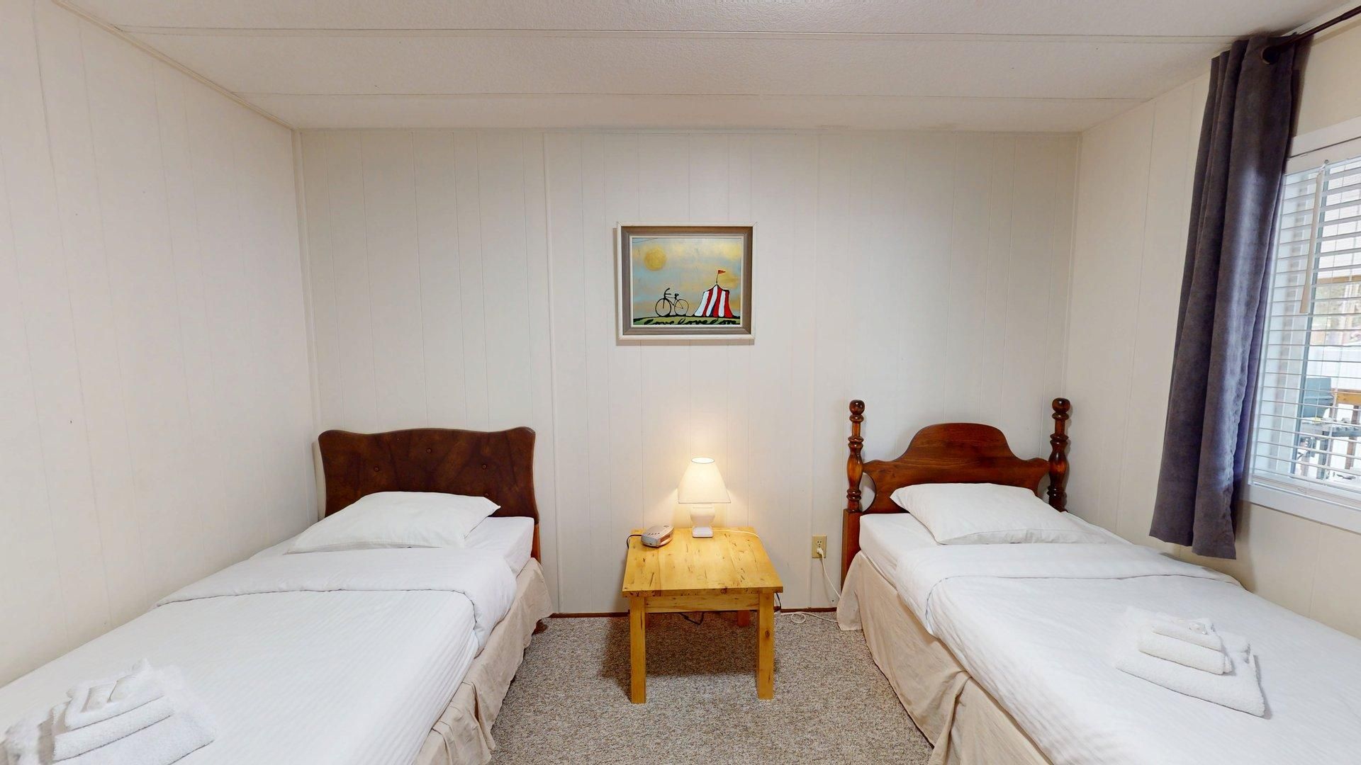 A small, clean room with two single beds, a nightstand with a lamp, and a picture on the wall.