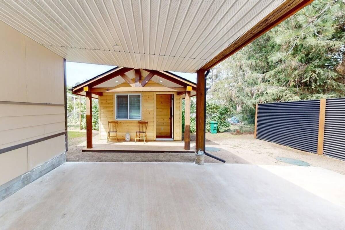 A covered outdoor seating area with a wooden structure, a window, and a view of a house.