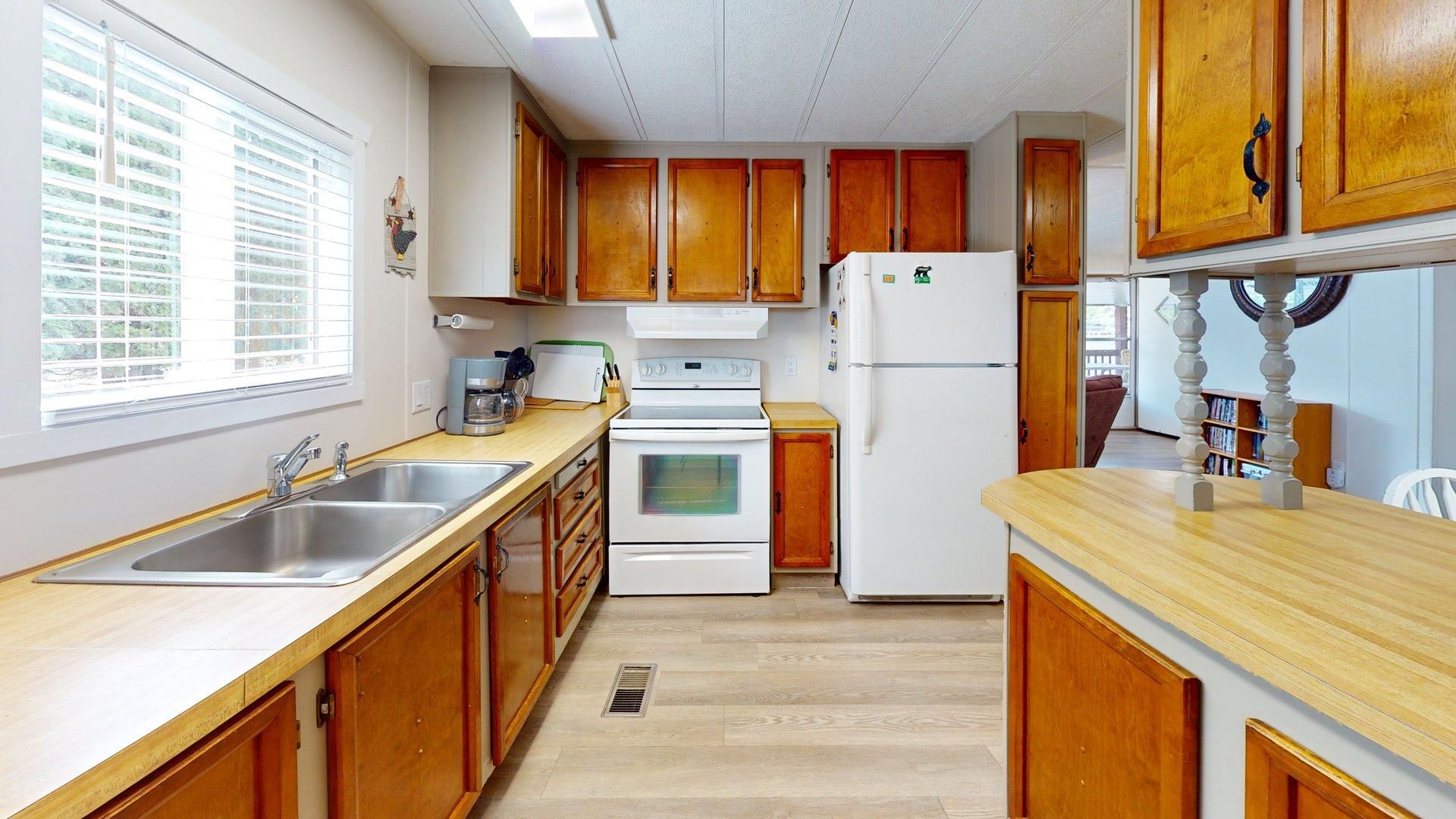 A kitchen with wooden cabinets, a stainless steel sink, a white stove, and a refrigerator.