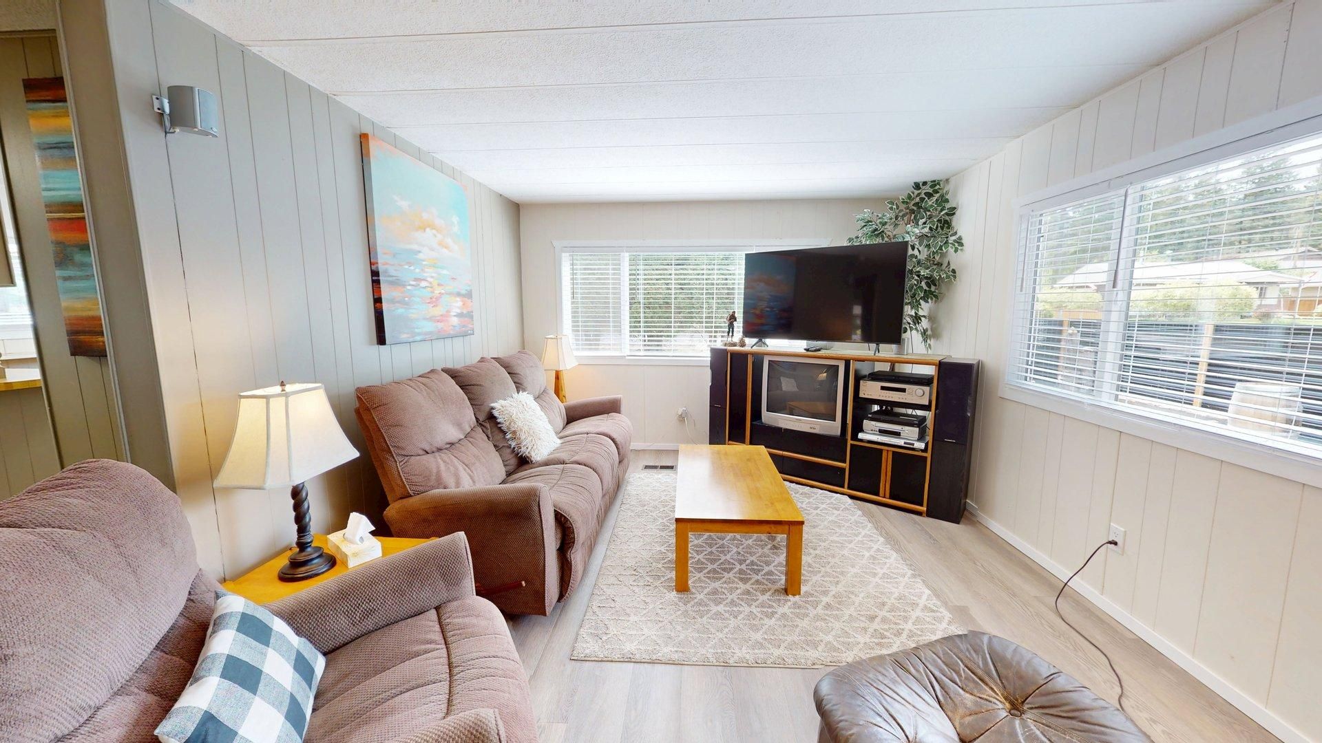 A living room with a sofa, a coffee table, a TV stand with a flat-screen TV, and a window with blinds.