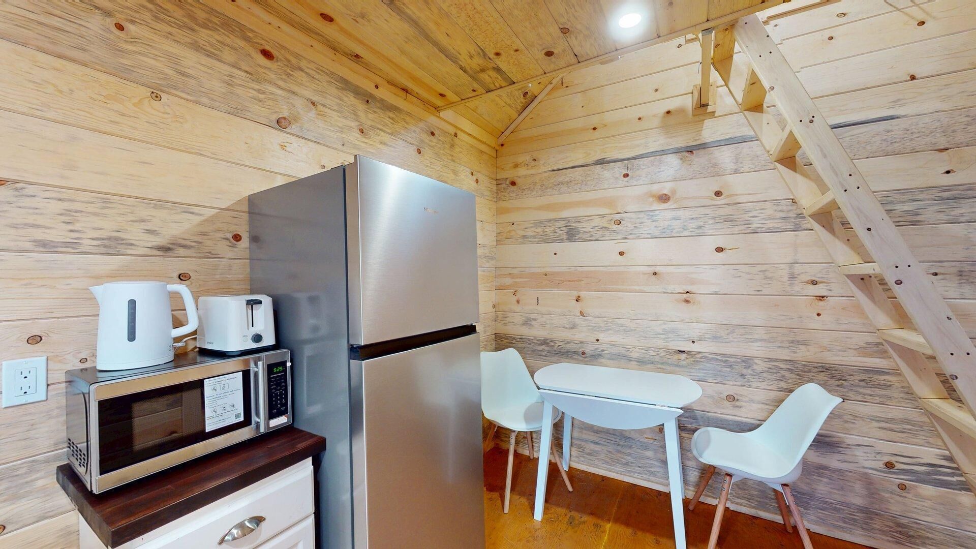Una cocina compacta equipada con refrigerador, microondas, tetera y tostadora, junto a un pequeño comedor con dos sillas y una mesa.