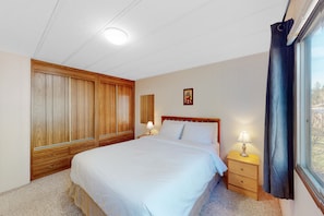 Un dormitorio con una cama grande, un armario de madera, lámparas de noche y una ventana con cortinas.