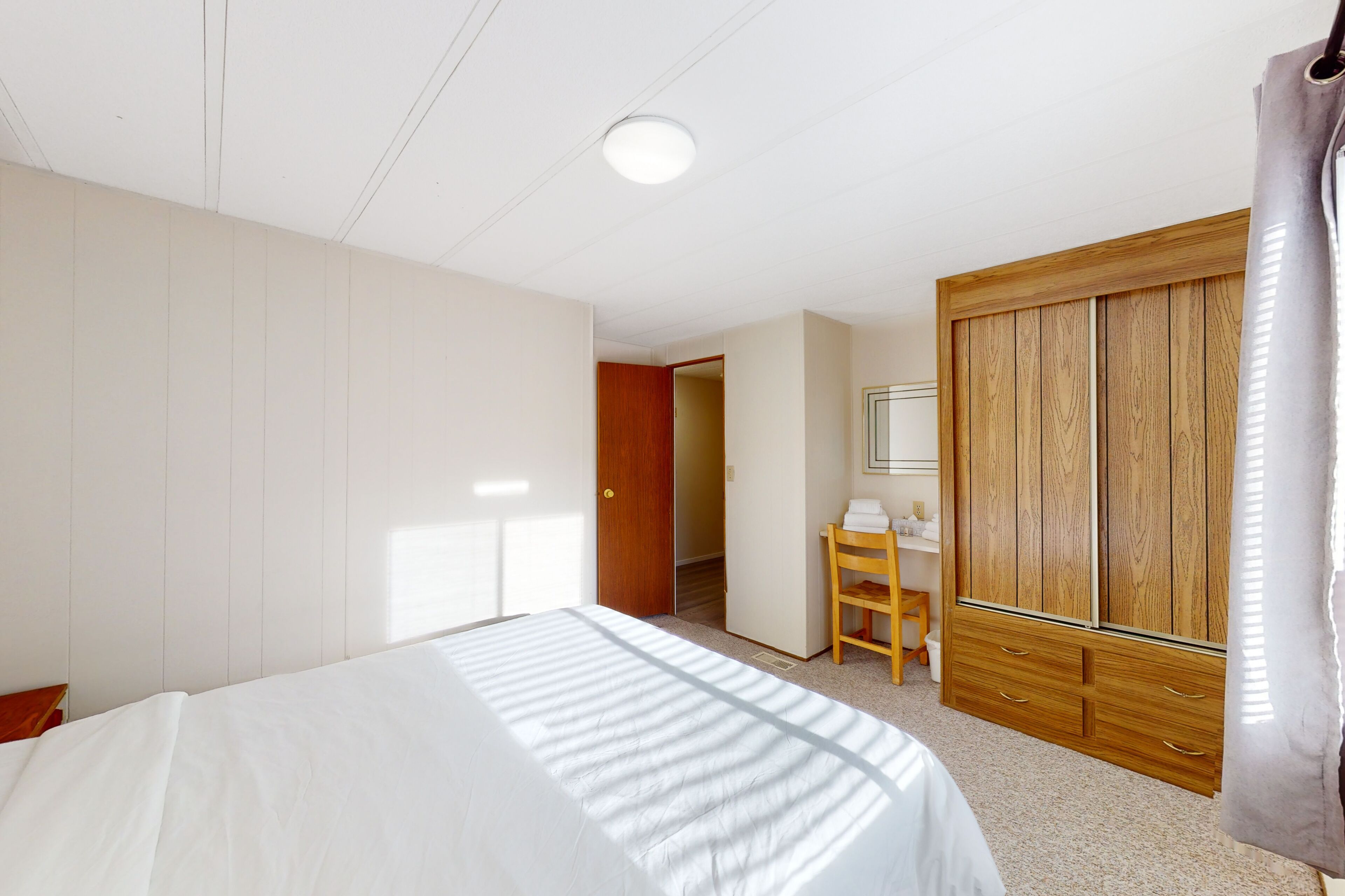 Une chambre à coucher comprenant un lit, une armoire en bois, un bureau avec une chaise et une porte donnant sur une autre pièce.