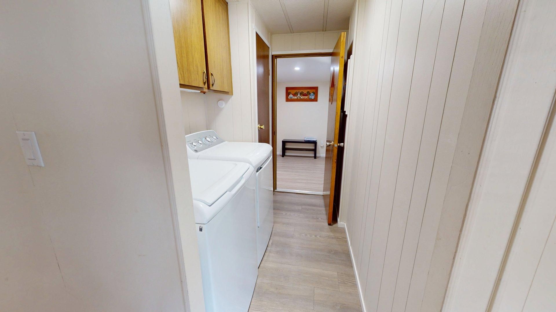 A narrow hallway with a washing machine, wooden cabinets, and a door leading to another room.