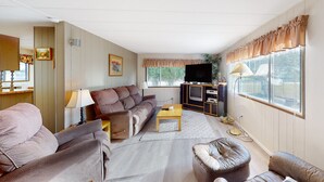 Uma sala de estar com sofá, poltrona, banqueta, televisão e um armário com televisão de tela plana.