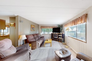 Una sala de estar con un sofá, un sillón, un reposapiés y una televisión.