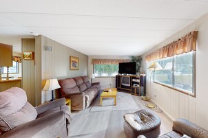 Uma sala de estar com sofá, poltrona, banqueta, televisão e um armário com televisão de tela plana.