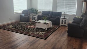 A living room with a dark wood floor, three black armchairs, a white coffee table, and a patterned rug.