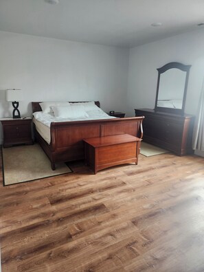 A bedroom with a wooden bed, nightstands, a dresser, and a mirror.