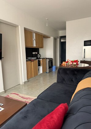 Ein modernes Wohnzimmer mit einer schwarzen Couch, einem Holzschrank und einer Küchenzeile mit Geräten.
