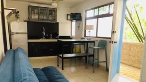 A living room with a sofa, a dining table with chairs, a kitchen area with cabinets, and a large window. - Apartment great location convenient parking (Mérida)