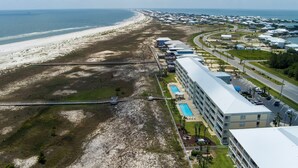 An aerial view of a coastal hotel with a long building adjacent to a beach, a swimming pool, and a parking area. - 3rd Floor ~ Amazing Views (Dauphin Island)