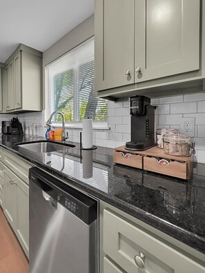 A modern kitchen with a dishwasher, coffee maker, and storage boxes. - The Green House-Adorable 2 bedroom house within the Baylor Bubble-Midterm only (Waco)