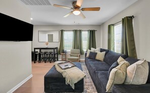 Ein Wohnzimmer mit einer Couch, Hocker und einem Essbereich mit Tisch und Stühlen.