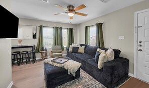 A living room with a sofa, ottoman, and a ceiling fan. - The Green House-Adorable 2 bedroom house within the Baylor Bubble-Midterm only (Waco)