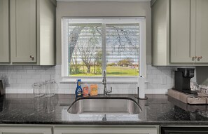 Eine Küche mit Spüle aus Edelstahl, einem Fenster mit Jalousien und einer Kaffeemaschine auf der Arbeitsfläche.