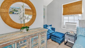 A room with a round mirror, blue upholstered furniture, a wooden cabinet, and a window with a white air conditioner. - Key West Steps to Duval, Truman Waterfront Park and Beach. Walk everywhere (Key West)