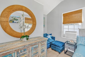 A room with a round mirror, blue upholstered furniture, a wooden cabinet, and a window with a white air conditioner. - Key West Steps to Duval, Truman Waterfront Park and Beach. Walk everywhere (Key West)