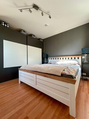 A bedroom with a bed, a nightstand, a lamp, a ceiling light fixture, and a wall-mounted projector.