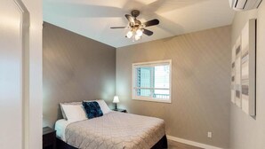 Quarto com cama, ventilador de teto, janela e mesa de cabeceira.
