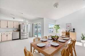 A modern kitchen with stainless steel appliances, a dining area with a wooden table set for six, and a view of a swimming pool through the glass doors. - Lakefront Family Escape with Pool | Near Disney (Davenport)