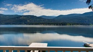 A calm lake with a wooden dock extending into the water, surrounded by forested hills. - Aussie Summer (Christina Lake)