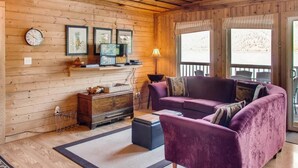 A cozy room with wooden walls, a purple sofa, a TV, and a window with a view. - Aussie Summer (Christina Lake)