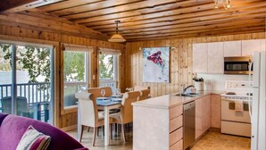 A wooden cabin with a dining area, kitchen, and a view of the outdoors. - Aussie Summer (Christina Lake)