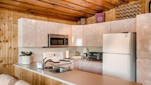 A kitchen with wooden walls, a stainless steel refrigerator, a microwave, a stove, and a sink. - Aussie Summer (Christina Lake)