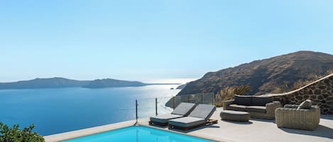 A pool with lounge chairs and a view of the sea.