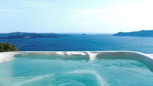 A clear view of a large body of water with distant landforms, a white infinity pool, and a clear sky.
