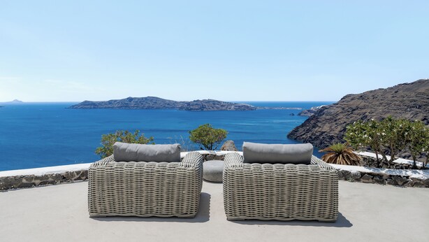 A seaside view with two wicker lounge chairs and a stone wall.