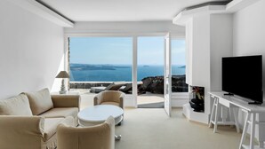 A modern living room with a sofa, coffee table, and TV, overlooking a scenic ocean view.