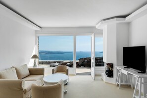 A modern living room with a sofa, coffee table, and TV, overlooking a scenic ocean view. - Neraé Santorini (Santorini)