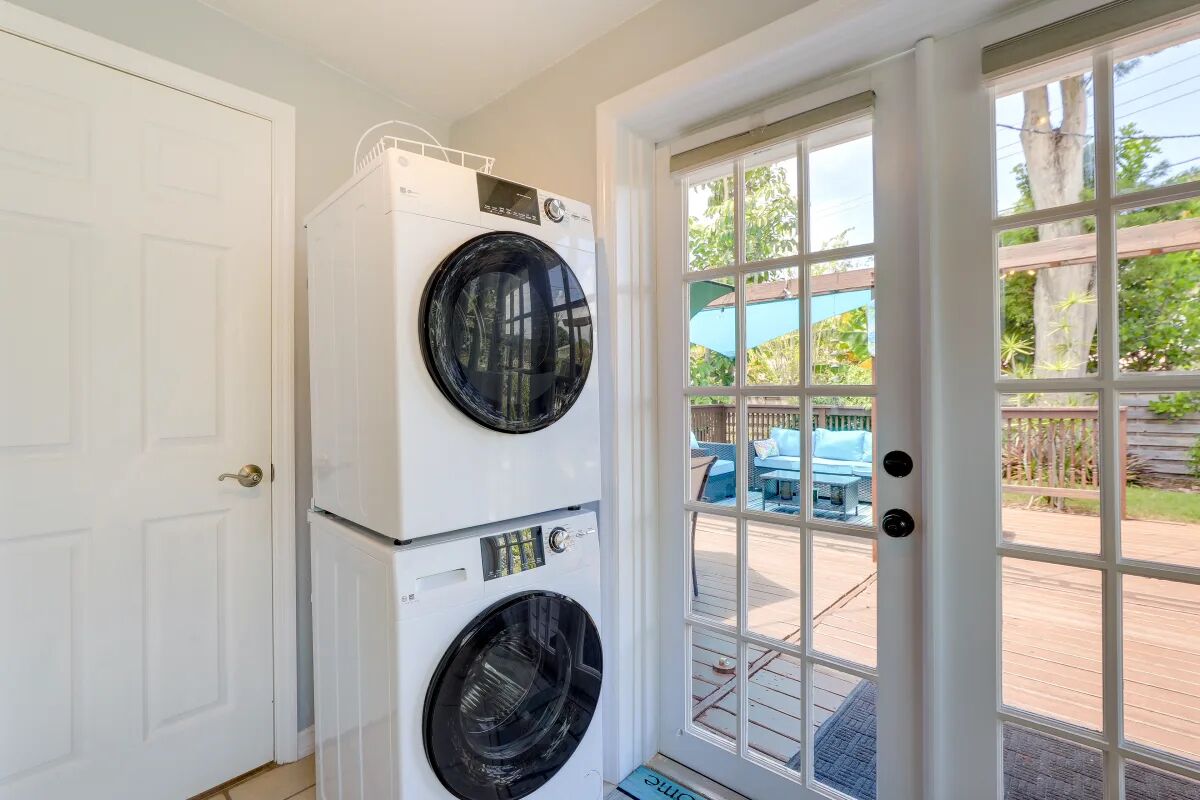 A laundry room with two stacked front-loading washers and dryers, a white door, and a view of an outdoor deck with furniture.