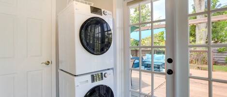 A laundry room with two stacked front-loading washers and dryers, a white door, and a view of an outdoor deck with furniture.
